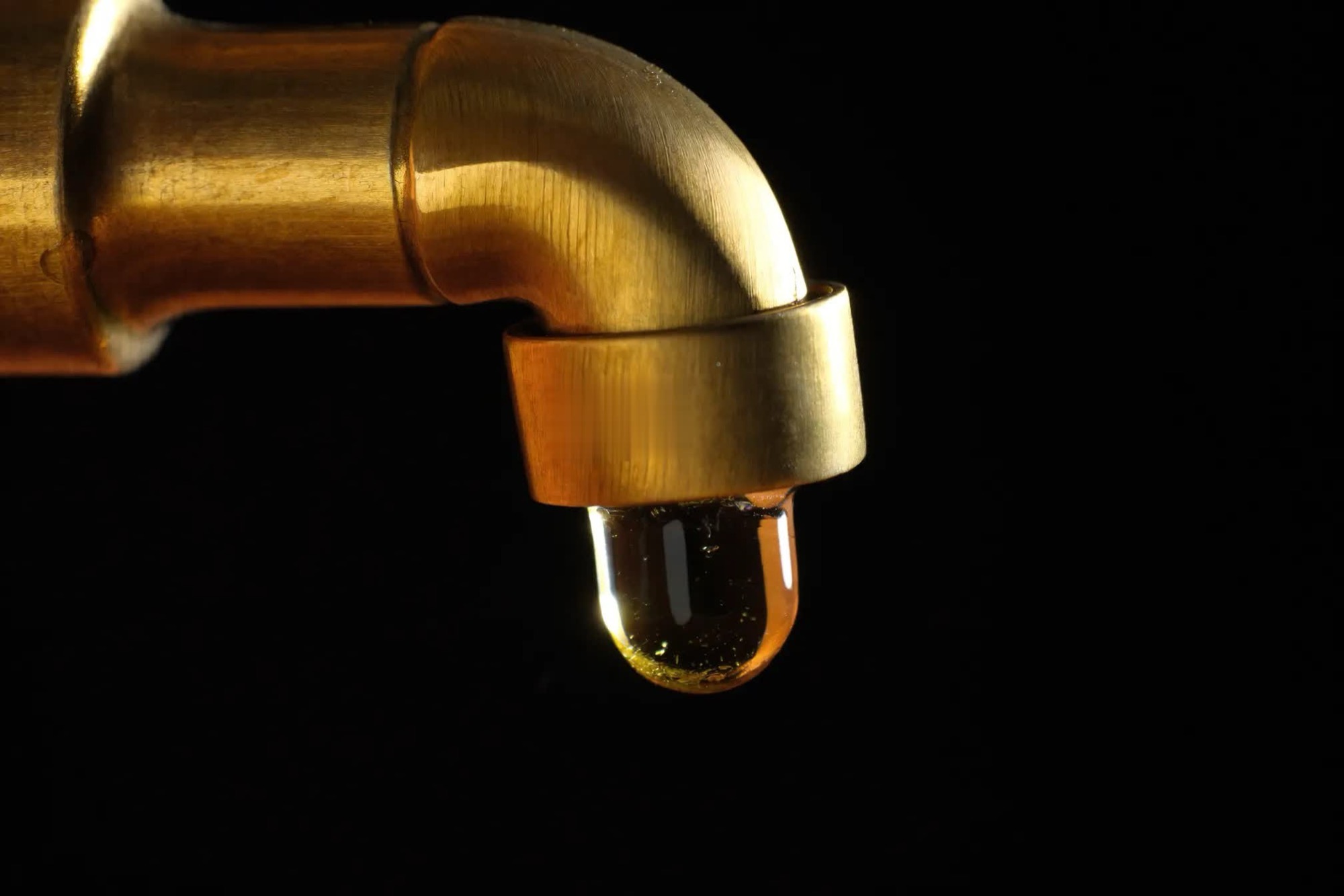 Une goutte tombe d’un robinet en laiton, sur fond noir